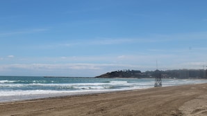 Una playa con una torre de salvavidas, orilla arenosa y edificios al fondo.