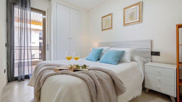Un dormitorio con cama, mesita de noche y ventana con cortinas.