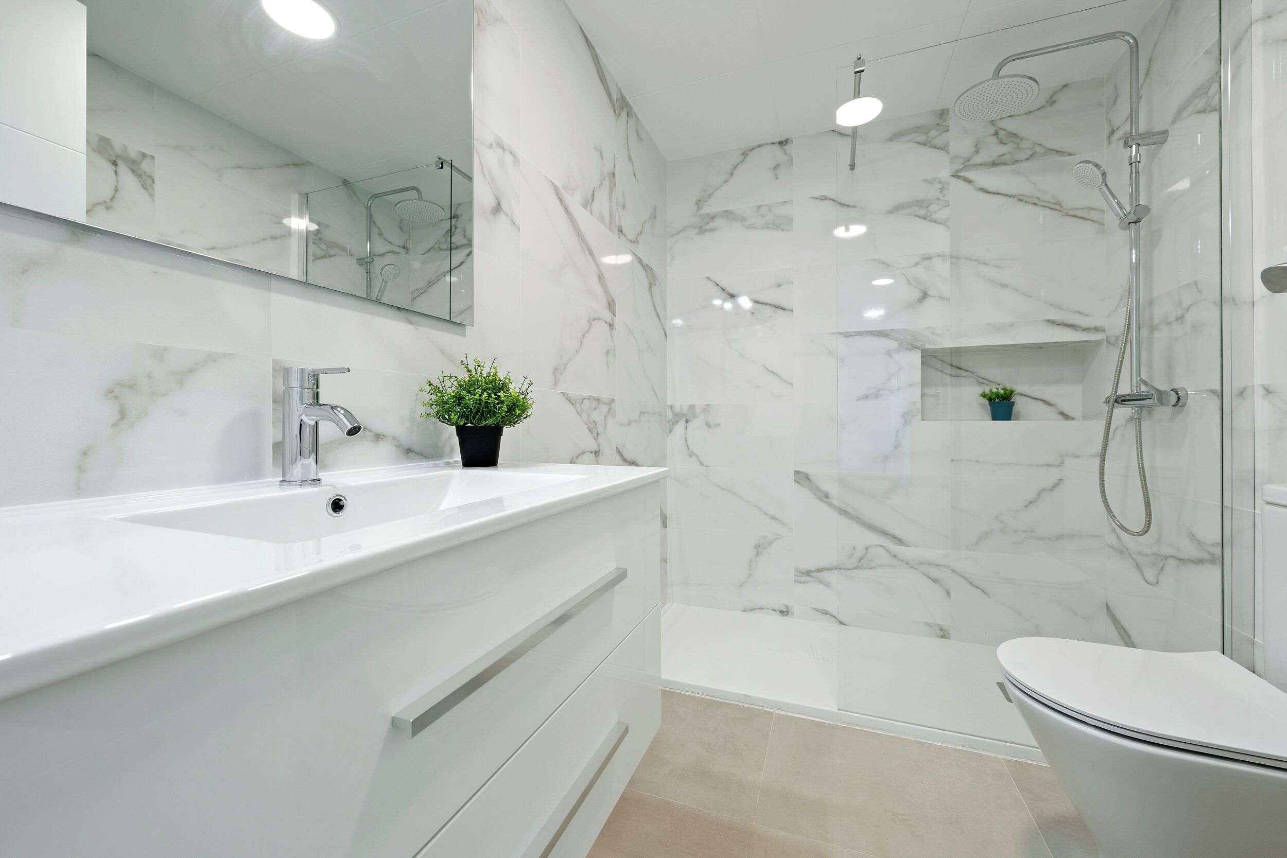 Un baño moderno con salpicadero de mármol, un lavabo blanco, un inodoro y una zona de ducha con mampara de cristal.