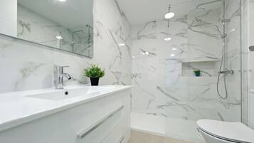 Un baño moderno con salpicadero de mármol, un lavabo blanco, un inodoro y una zona de ducha con mampara de cristal.