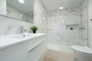 Ein modernes Badezimmer mit Marmor-Spritzschutz, einem weißen Waschbecken, einer Toilette und einer Duschkabine.