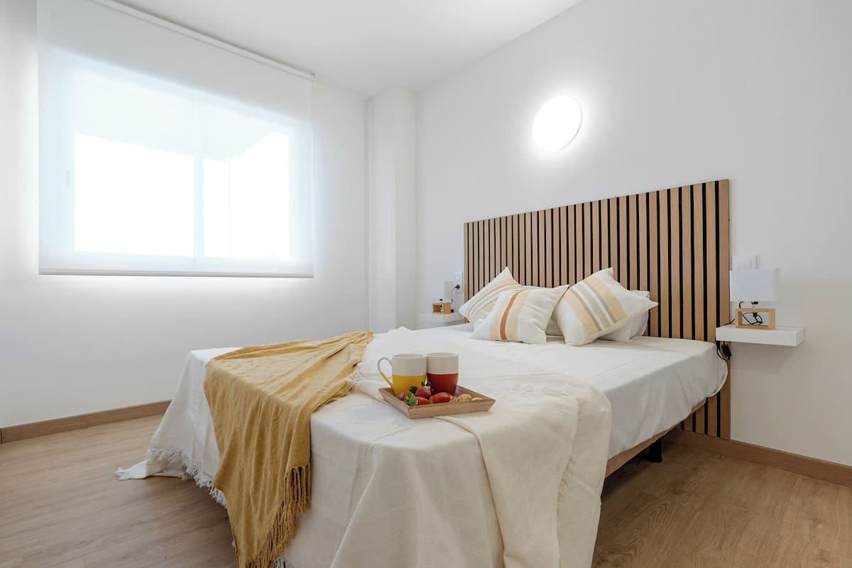 A neatly arranged bedroom with a bed, bedside tables, a bedside lamp, a window, and a bedside shelf.