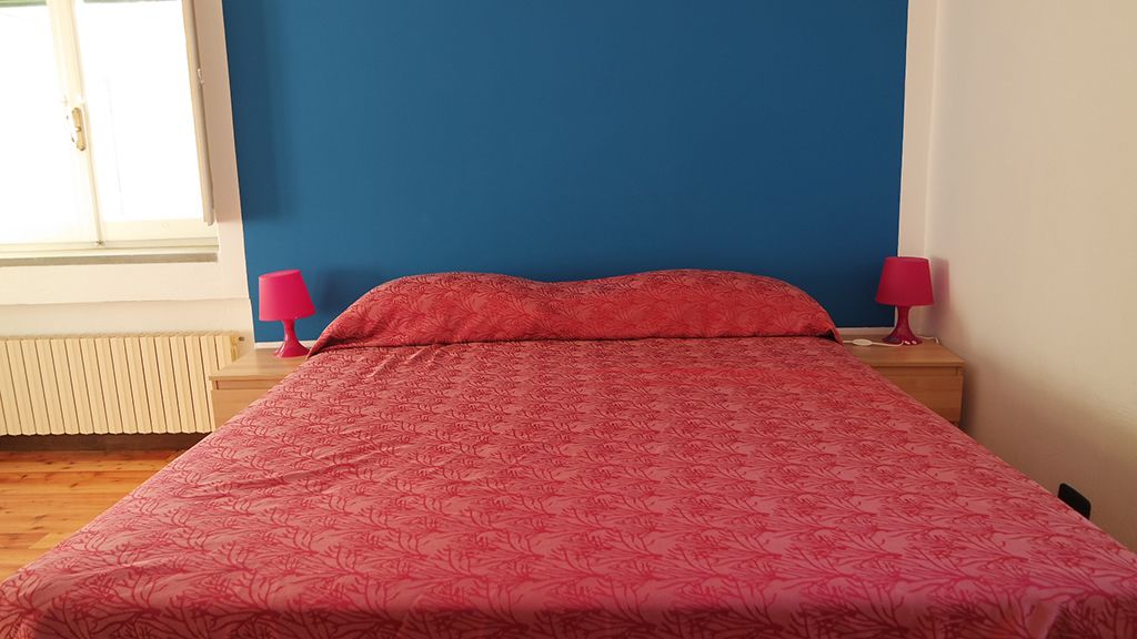 Een bed met een rode bloemenprint, twee bedlampjes en een raam met jaloezieën.