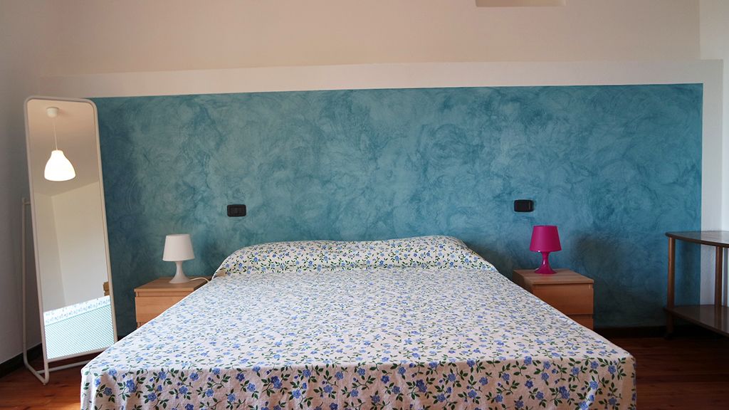 A bedroom with a bed, two bedside tables, a nightstand, a lamp, and a wall unit.