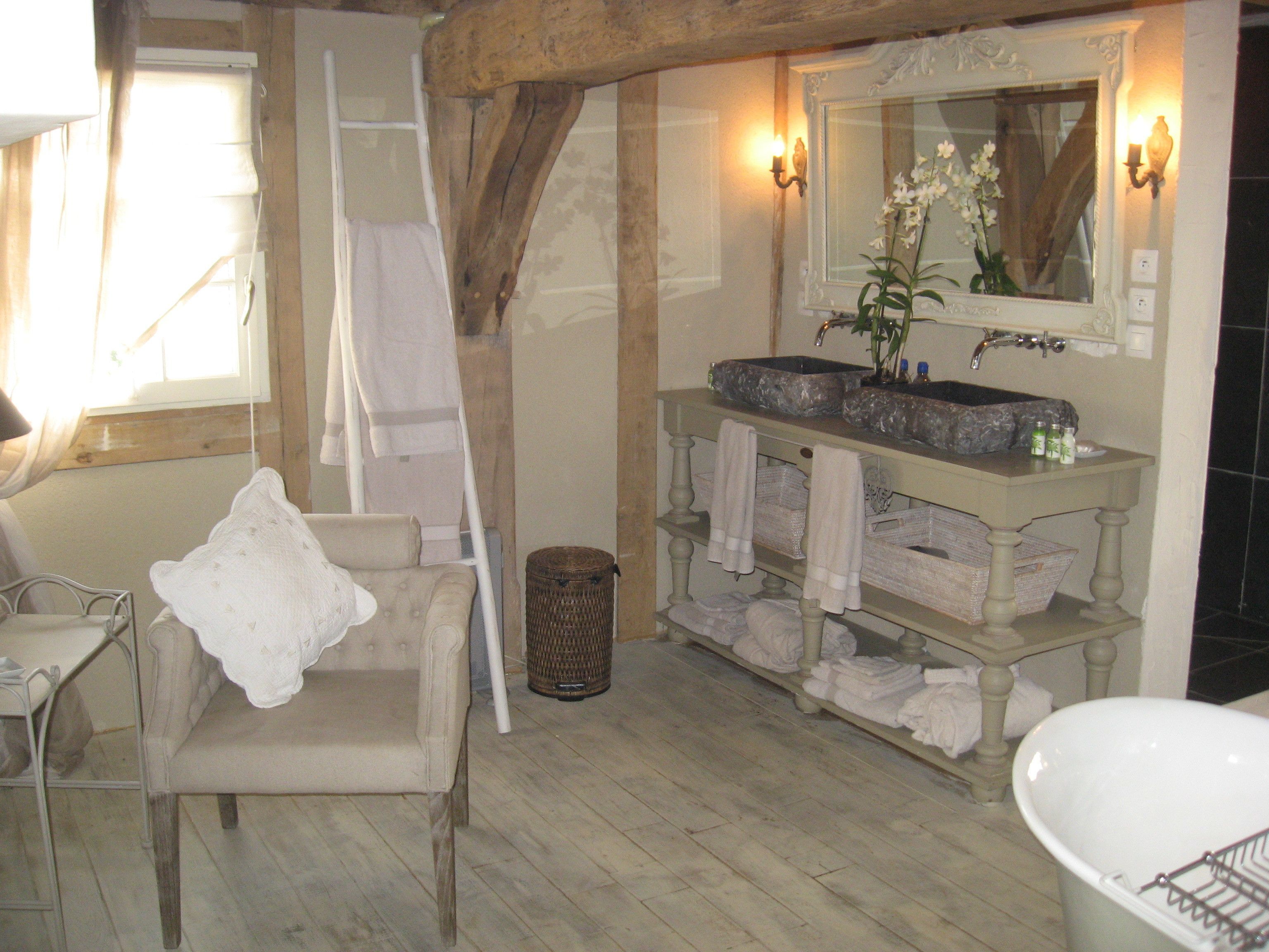 Ein Badezimmer mit einer großen Badewanne, einem Schminktisch mit Spiegel und einem Sessel. Auf dem Boden liegen Handtücher und ein Korbwannenmodell.