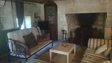Een gezellige woonkamer met een stenen openhaard, een bank, een gestreept fauteuil en een salontafel.