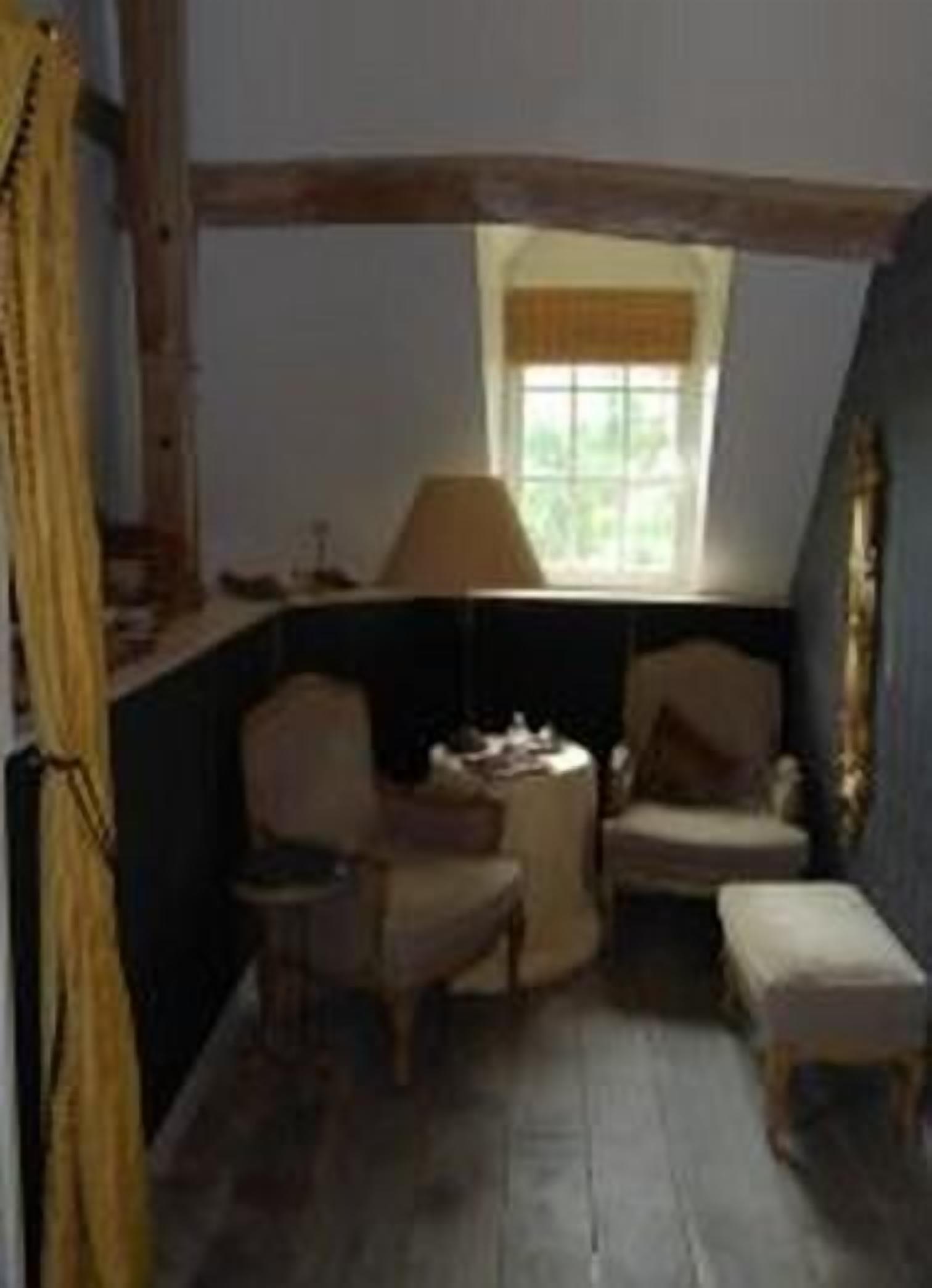A room with a sloped ceiling, a window with a curtain, two chairs, a small table, and a bench.