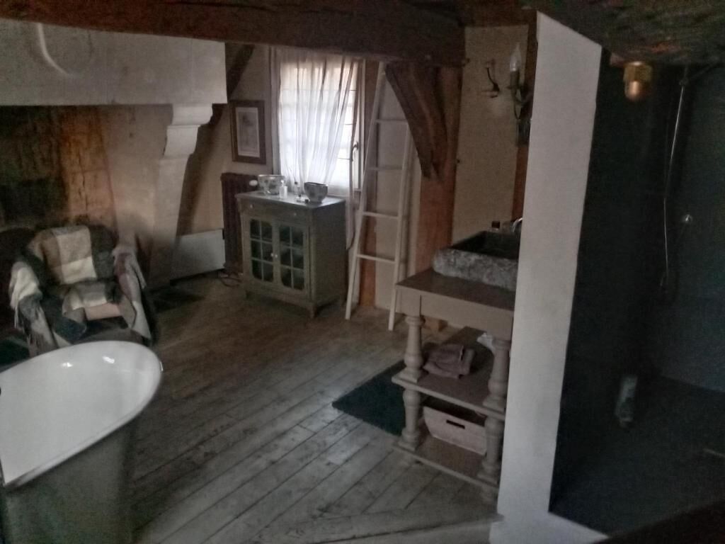 A room with a wooden floor, a white bathtub, a wooden cabinet, and a door with a window.