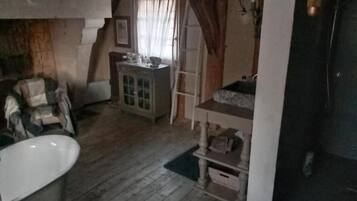 A room with a wooden floor, a white bathtub, a wooden cabinet, and a door with a window.