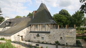 A stone house with a steeply pitched roof, a small balcony, and a garden area with gravel paths and potted plants. - Chambres d'Hôtes Le Mouton (Blaison-Saint-Sulpice)