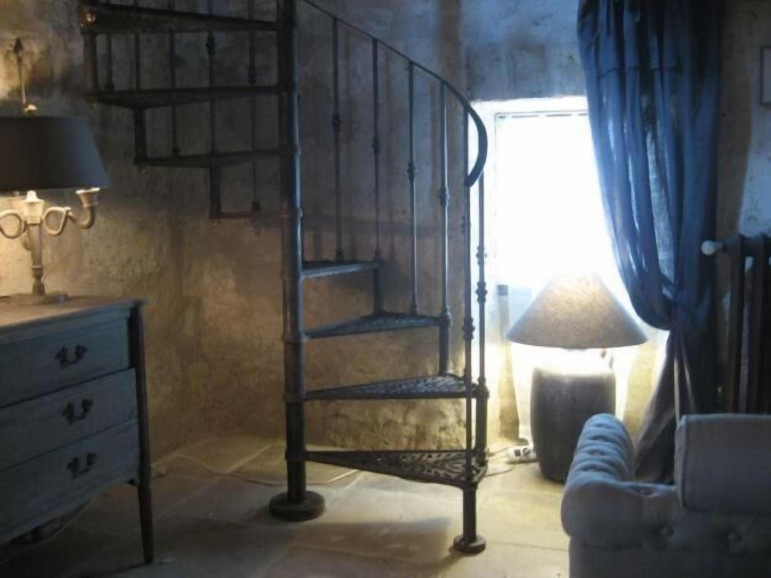 Une pièce avec un escalier en colimaçon en métal, une commode à tiroirs, une lampe et un radiateur.
