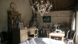 A rustic room with a bed, a wooden cabinet, a chandelier, a dining table with chairs, and a clock on the wall. - Chambres d'Hôtes Le Mouton (Blaison-Saint-Sulpice)