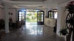 A spacious lobby with a polished marble floor, a grand entrance with a large arched doorway, and a view of the outdoor garden. - Hotel Praia Do Conde (Conde)