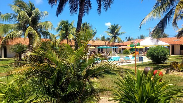 A pool area with lounge chairs and umbrellas, surrounded by palm trees and greenery. - Hotel Praia Do Conde (Conde)