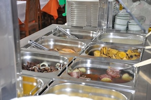 Buffet com diversas opções de comida, incluindo carnes, legumes e frutas.