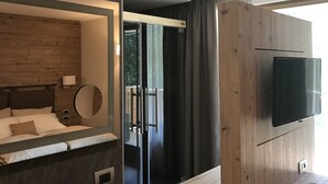 Un dormitorio moderno con cabecera de madera, una cama grande, un espejo en la mesita de noche y un televisor montado en la pared.