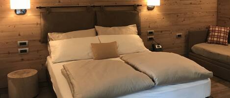 A wooden cabin room with a bed, two bedside lamps, a nightstand, and a small round stool.