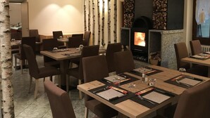 Un restaurante con mesas y sillas de madera, una chimenea y decoración con ramas de abedul.
