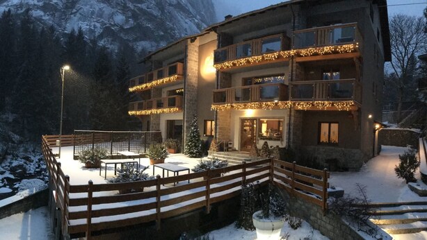 Un edificio de varios pisos con balcones, una terraza de madera y un paisaje cubierto de nieve.