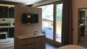 Una habitación moderna con una unidad de entretenimiento de madera, un televisor y un ventanal corredera que da a un balcón con mobiliario exterior.