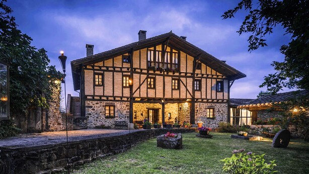 A traditional half-timbered building with stone walls and wooden beams, featuring a stone pathway and a well-maintained lawn. - Caserio Iruaritz (Amurrio)