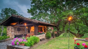 A rustic stone building with a tiled roof, surrounded by lush greenery and flowering plants. - Caserio Iruaritz (Amurrio)