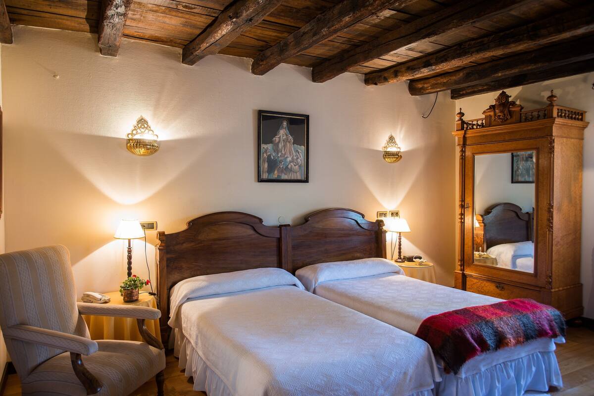 A double bed with a wooden headboard, a chair, a bedside table with a lamp, and a mirror.