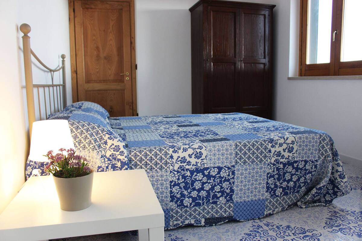 A bedroom with a bed, a nightstand, a potted plant, and two wooden doors.