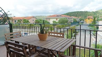 Un balcone con mobili in legno e una pianta in vaso, con vista su una zona residenziale con case e una strada.