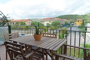 Un balcón con mobiliario de madera y una planta en maceta, con vistas a una zona residencial con casas y una calle.