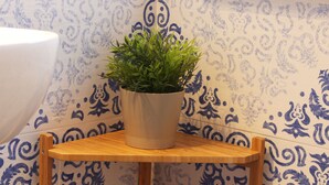Un baño con un lavamanos blanco, una planta en maceta sobre un taburete de madera y baldosas azules con motivos.