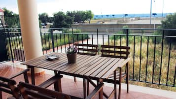 Un tavolo e sedie di legno su un balcone con vista sul mare e un vialetto.