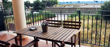 A wooden table and chairs on a balcony with a view of the sea and a pathway.