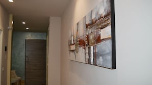 A hallway with a modern abstract painting on the wall, a closed door, and a small table with a chair. - B&B Jolie Center (Pescara)