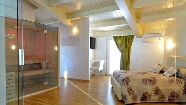 A modern bedroom with a glass partition, a bed with patterned bedding, a desk, and a television. - B&B Jolie Center (Pescara)