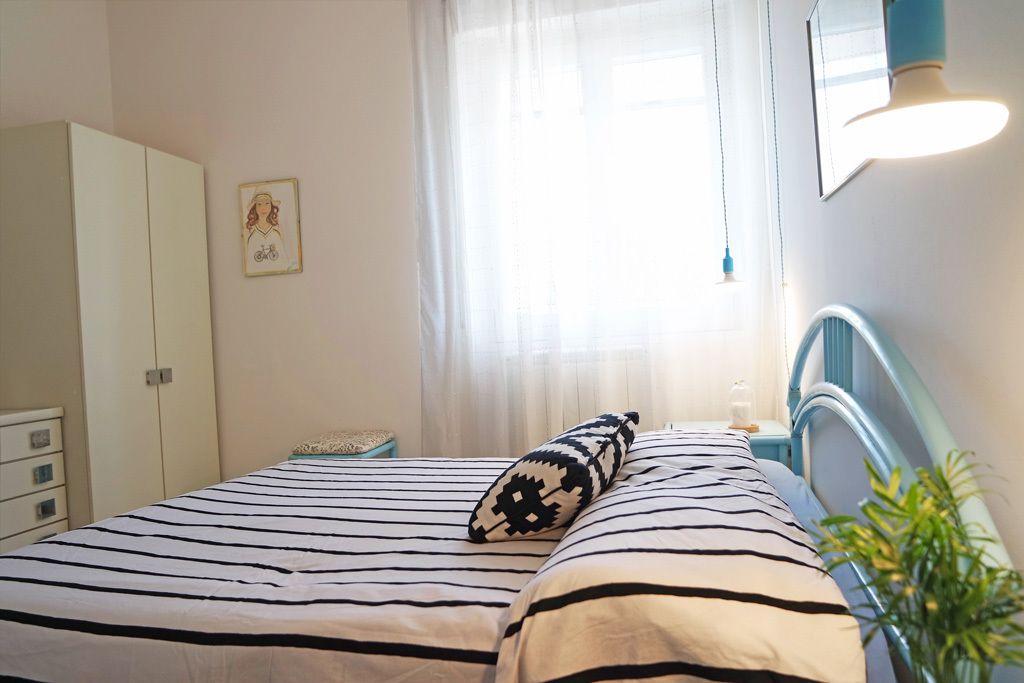 Un dormitorio con cama, mesita de noche, armario y ventana con cortinas.