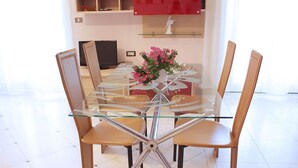A modern dining area with a glass-top table and wooden chairs. - Casa Eleatica (Ascea)