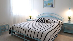A bedroom with a bed, a bedside table, a nightstand, a window with curtains, and a wall-mounted picture. - Casa Eleatica (Ascea)