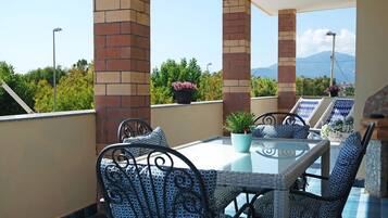 Eine Dachterrasse mit einem Glastisch und Korbstühlen, umgeben von Ziegelstützen und Topfpflanzen.