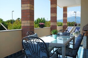 Une terrasse sur le toit, dotée d’une table en verre et de chaises en osier, entourée de piliers en briques et de plantes en pot.