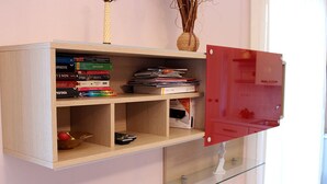 A wall-mounted wooden shelf with books, a remote control, and a vase with dried plants. - Casa Eleatica (Ascea)