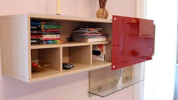 Eine Wandablage mit Büchern, einer Fernbedienung und einer Vase mit Trockenpflanzen.