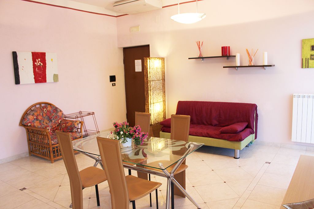 A modern living room with a glass dining table, a red sofa, and a wicker chair.