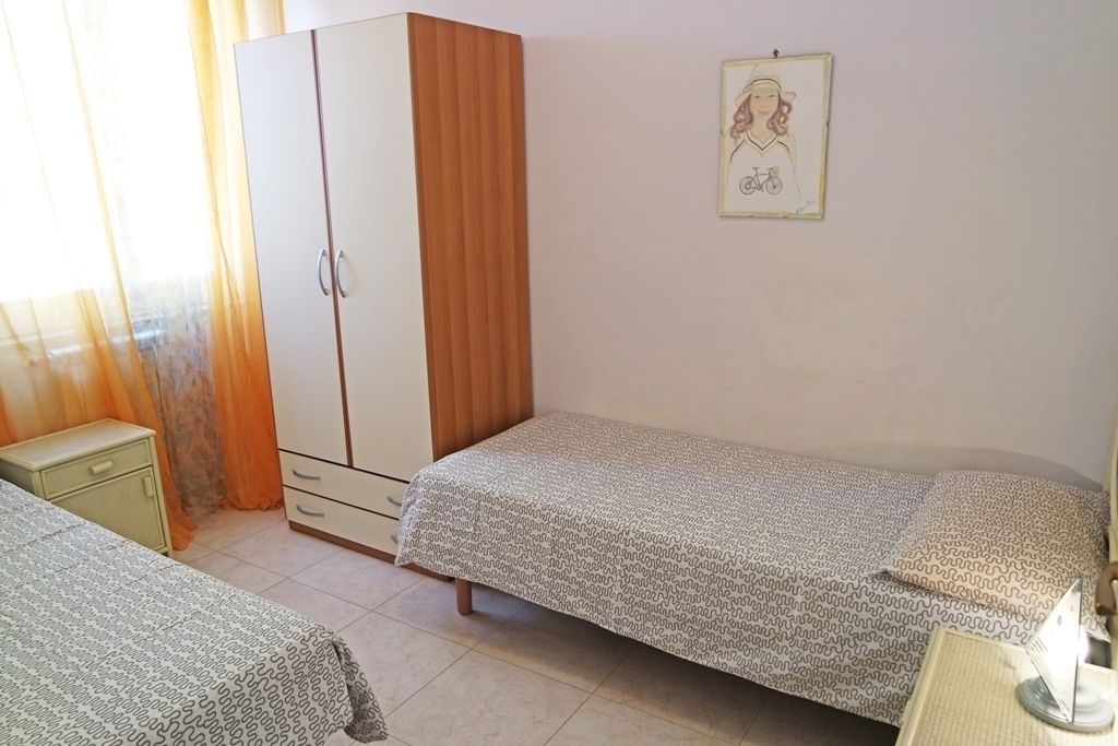 A bedroom with two single beds, a wardrobe, a small bedside table, and a framed picture on the wall.