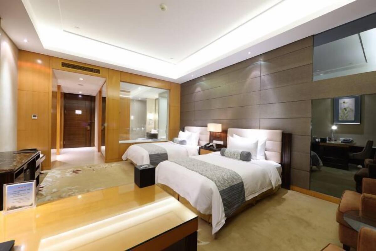 A modern hotel room with two beds, a desk, a chair, and a large mirror.