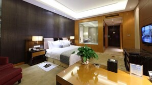 A hotel room with a bed, bedside table, lamp, TV, and a plant. - Huifeng Hotel (Shuyang)