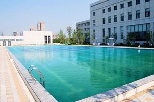 Una piscina con agua cristalina azul, rodeada por una terraza con baldosas y sillas de descanso.