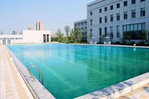 A swimming pool with a clear blue water, surrounded by a tiled deck and a building in the background. - Huifeng Hotel (Shuyang)