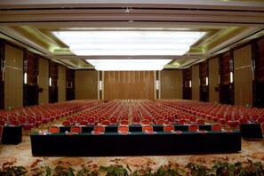 Un salón de conferencias con filas de sillas, una mesa larga y piso alfombrado.