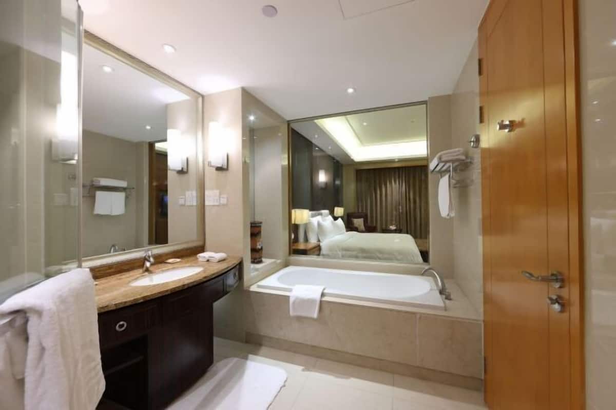 A modern bathroom with a large mirror, a bathtub, a vanity with a sink, and a wooden door.